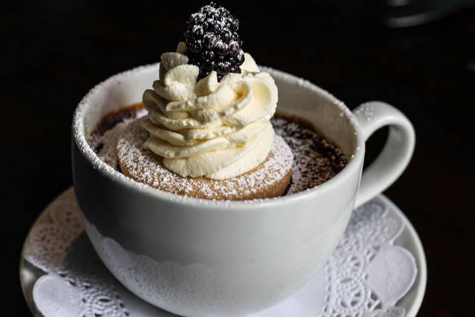 A chocolate dessert in a teacup with whipped cream and a blackberry